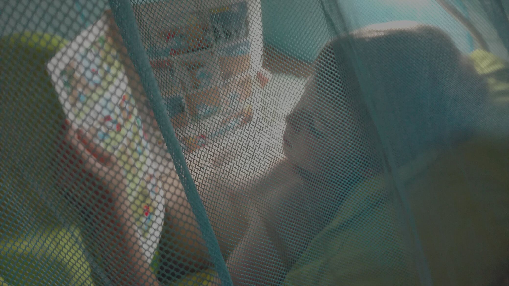 Someone reading on a phone, seen through a mesh curtain